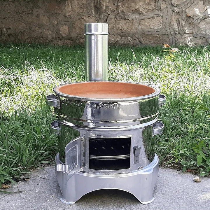 The HAKAN Portable Guvec Mangal Soba Clay Grill Barbecue Stove is a polished 15-inch chrome stove with a central chimney and an open door, ideal for outdoor cooking. Its clay interior captures the essence of a Turkish barbecue set, perfect for versatile cooking opportunities in nature settings.