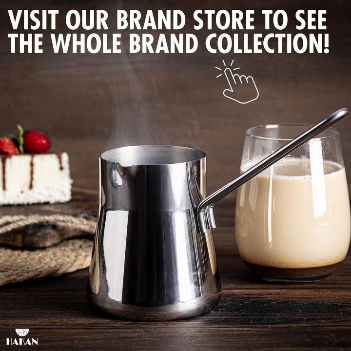 A stainless steel coffee pot on a wooden table, with milk and cake. Text above reads: "Visit our brand store to see the whole brand collection!"