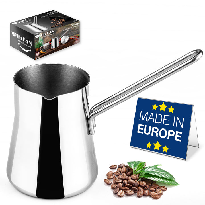 A stainless steel turkish coffee pot with a long handle beside coffee beans and a "Made in Europe" sign; product packaging in the background.