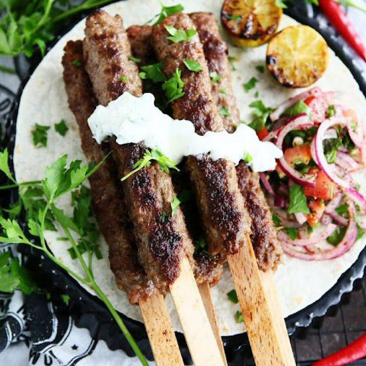 Served on flatbread with yogurt, grilled kebabs on Hakan 9.8-inch wooden skewers are garnished with cilantro and accompanied by grilled lemon halves and a spiced red onion salad.